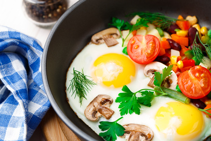 Fried eggs in a pan with vegetables and mushrooms