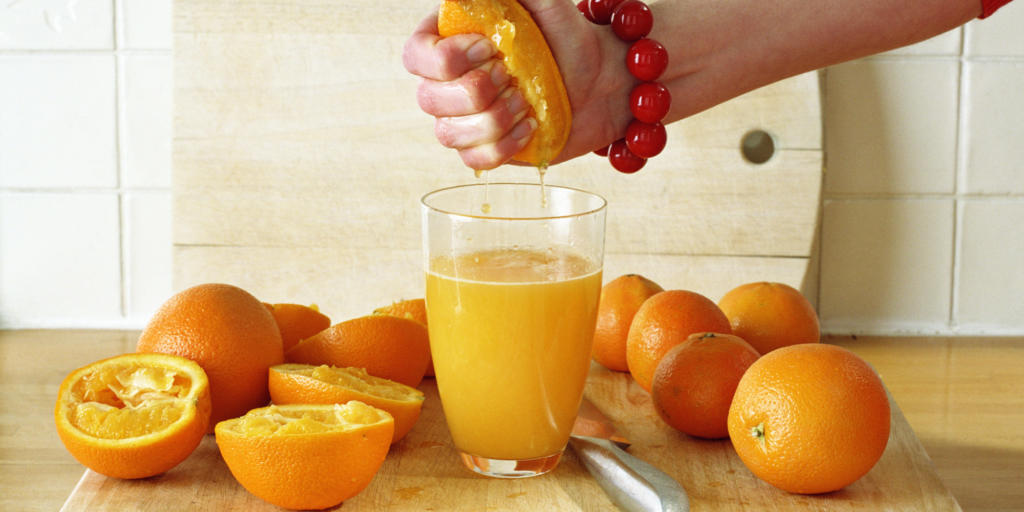 Woman squeezing cut orange into glass on chopping board, close-up
