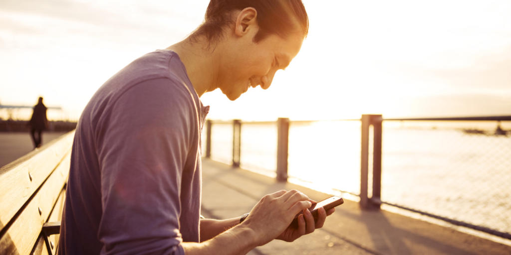 Young Man Using Smartphone In Park At Sunset