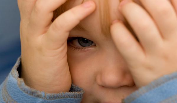 Boy peeking from behind his hands.